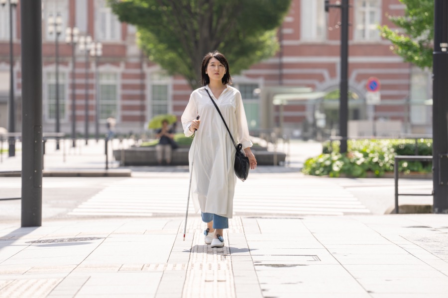右手に白杖を持ち、左手には何も持たずに歩いている女性の画像