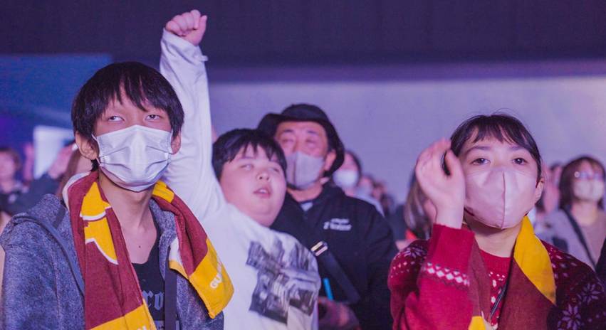 会場の熱気の中で手を挙げ、全身を使って音楽を楽しむ参加者と同行者