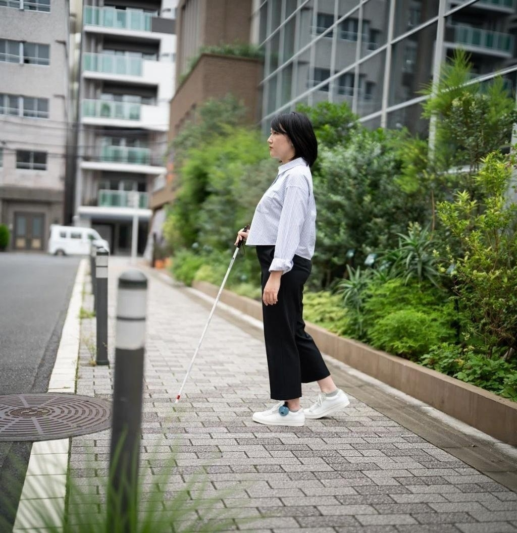はくじょうを持った女性が、あしらせを付けて歩道を歩いている